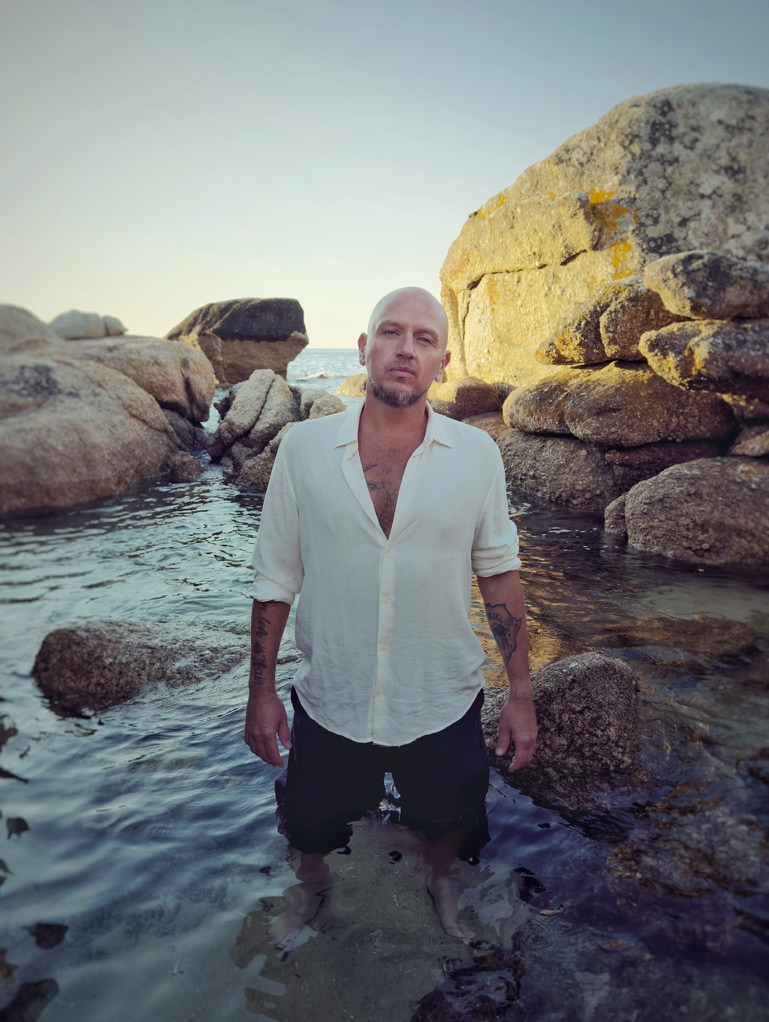 ARD matthews standing among rocks with a guitar